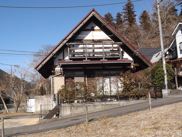 診療所とバス停の前で名栗川の傍に建つ合掌造り住宅 おちあい不動産